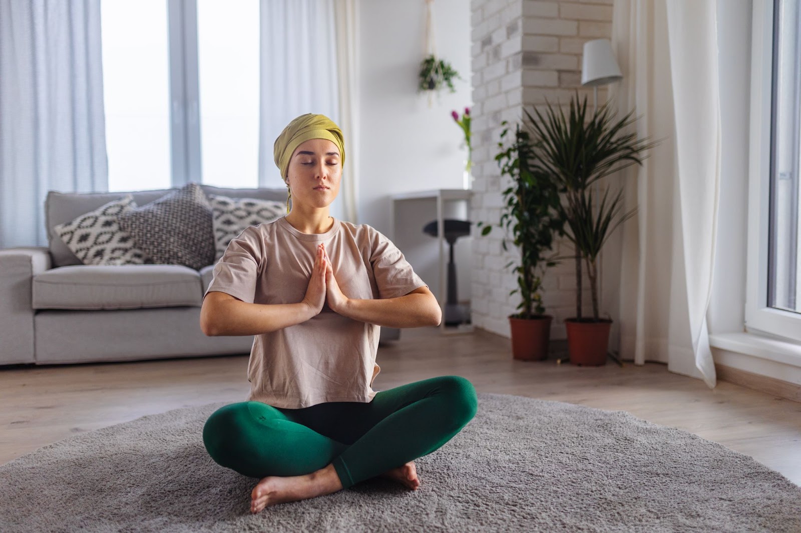 Jovem mulher com câncer fazendo ioga e meditando em seu apartamento.