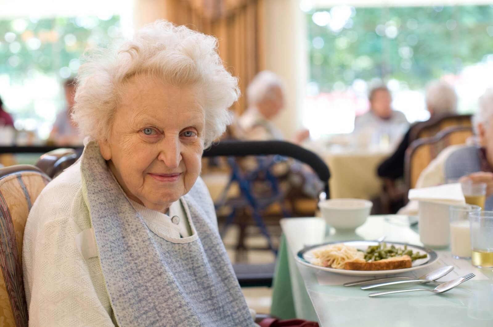 A smiling older adult sitting at a dining table while enjoying a meal in assisted living.