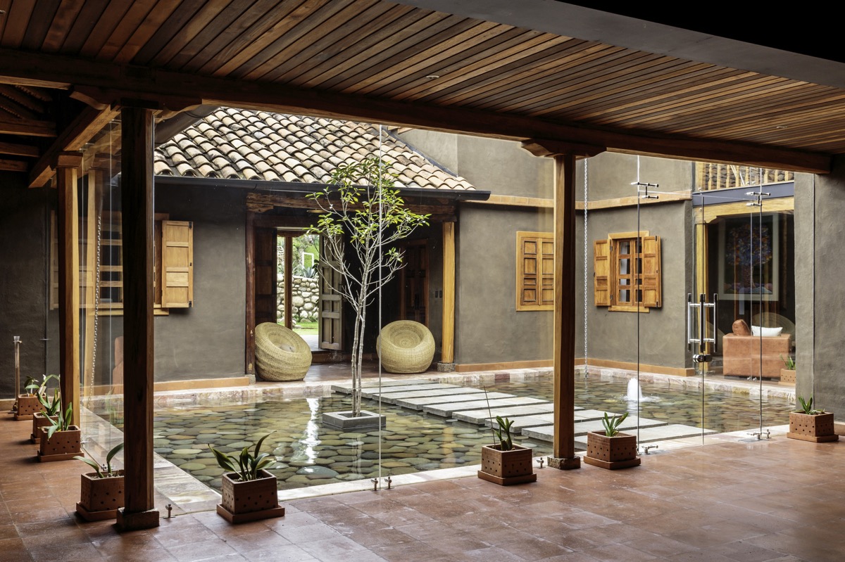 A tranquil indoor courtyard with a pebbled pool and a small tree at the center showcases skilled craftsmanship.