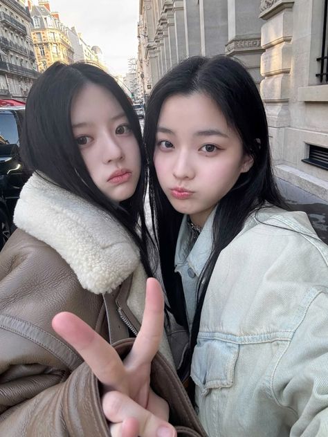 This  contain an image of ILLIT Minju and BOYNEXTDOOR Leehan standing next to each other giving the peace sign with their fingers in front of them