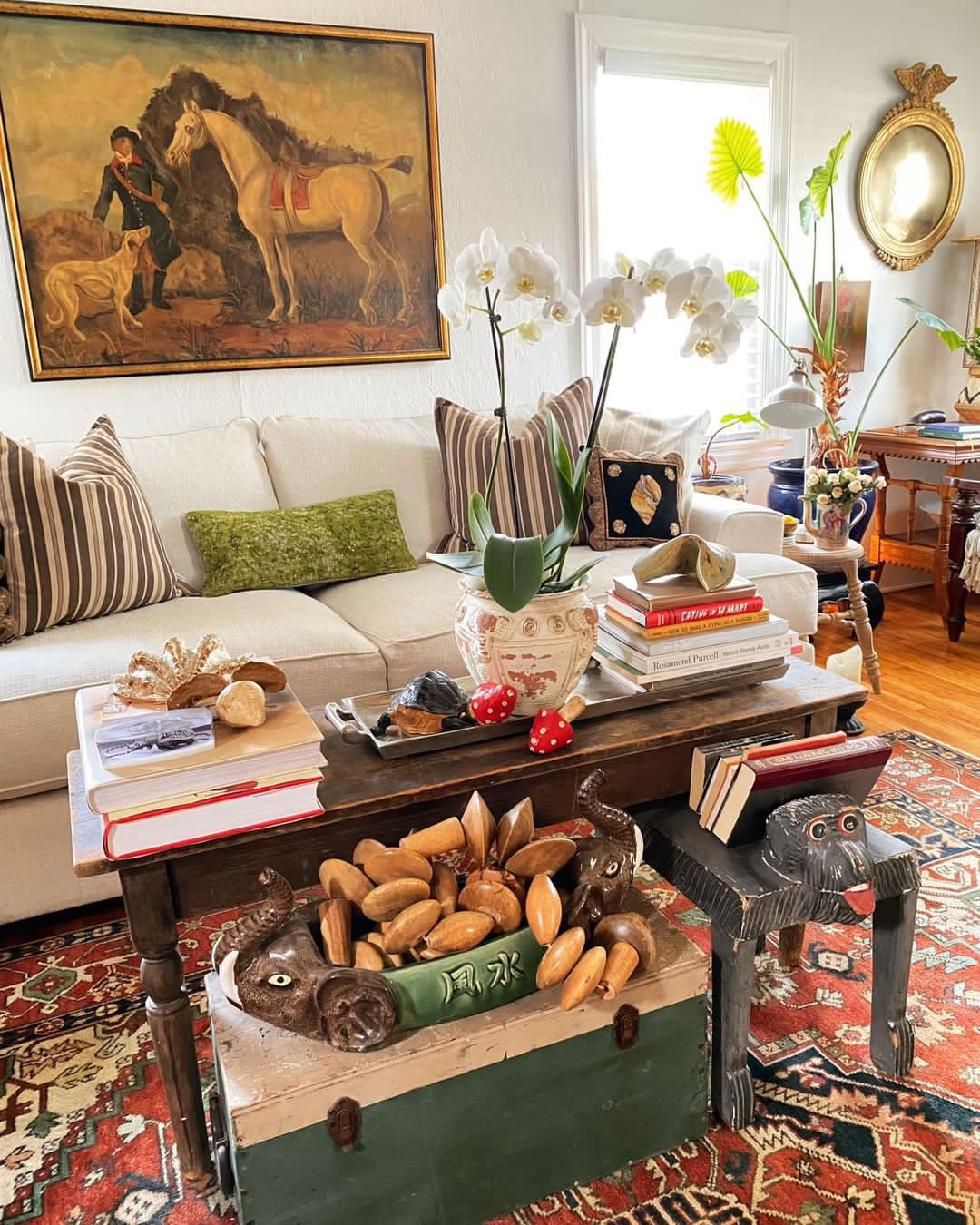 An oversized equestrian painting hangs above a cream white sofa while a mixed assortment of shells and other artifacts decorate the coffee table