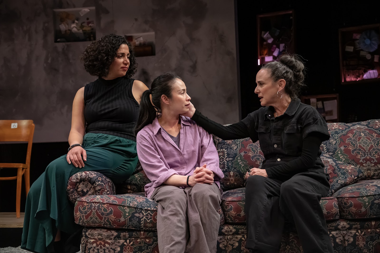 Three actors sit on a couch on a theater stage having an emotional coversation.