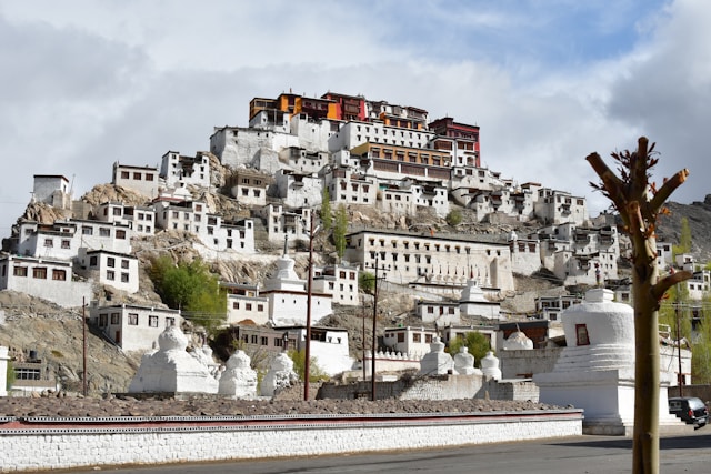 A picturesque view of a monastery complex built on a hillside, featuring white buildings with colorful rooftops, showcases Indian architecture and traditional building techniques.