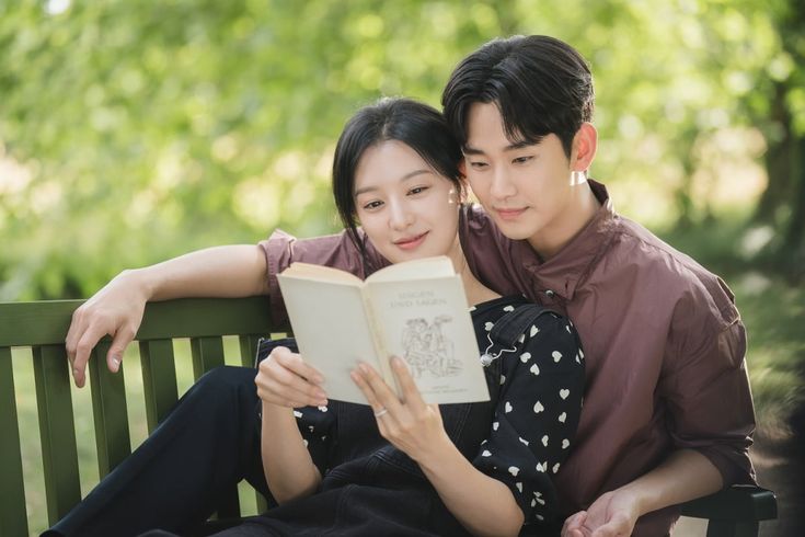 This contain Kim Soo Hyun and Actress Kim Ji Won are sitting on a bench and reading a book while looking at the camera