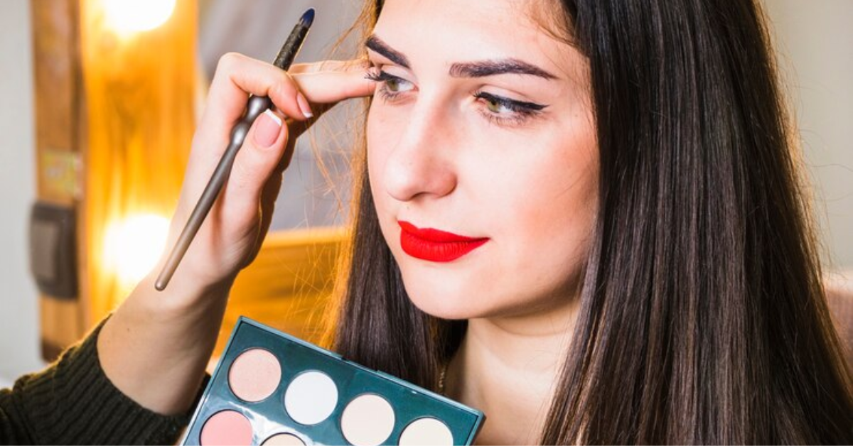 A woman skillfully applies eyeshadow to enhance her facial features in a well-lit setting.