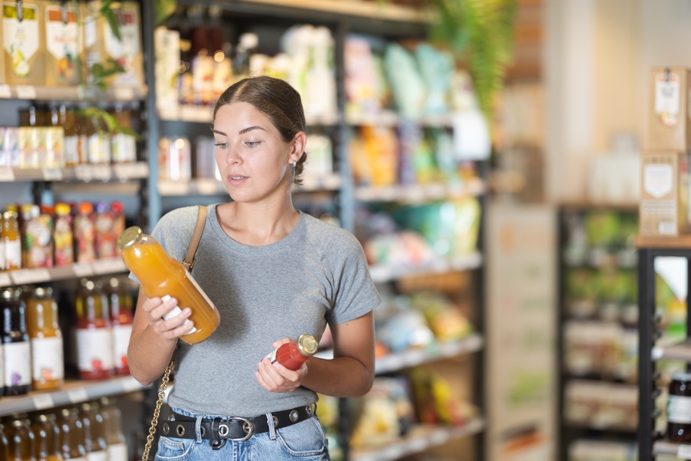 Young woman reading different brands’ product ingredients in a store to spot potential greenwashing signs.