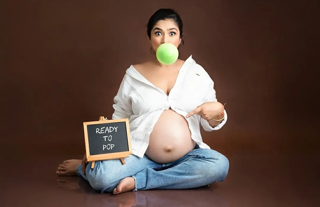 Pregnant woman sitting with pregnancy reveal board on a seasonal maternity photoshoot.