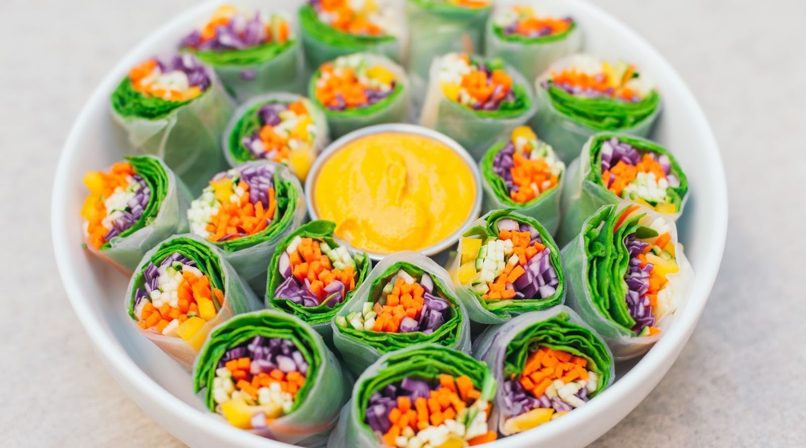 Healthy vegetarian spring rolls with colorful fresh vegetables including carrots, cabbage, and greens, served with a vibrant dipping sauce on a white plate. A perfect choice for those seeking nutritious and delicious options at healthy restaurants in Mississauga. Recommended by registered dietitians.