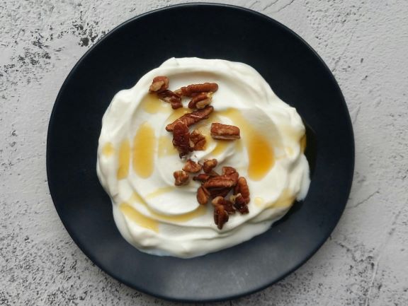 A healthy weight gain snack bowl of Greek yogurt, honey, and dates on a wooden table top. 