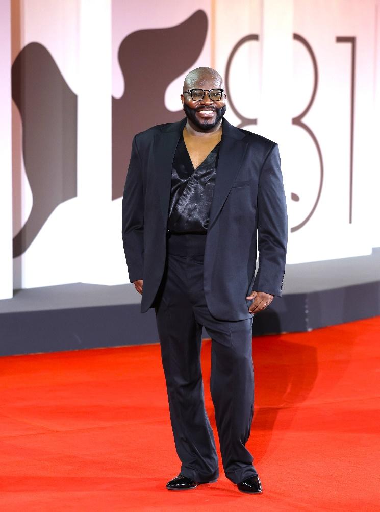 A person in a suit walking on a red carpet

Description automatically generated