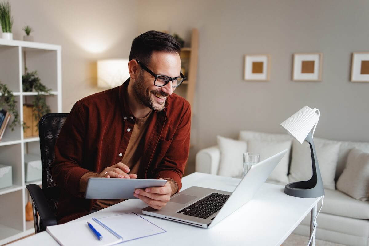 Employee using a tablet while happily looking at his laptop