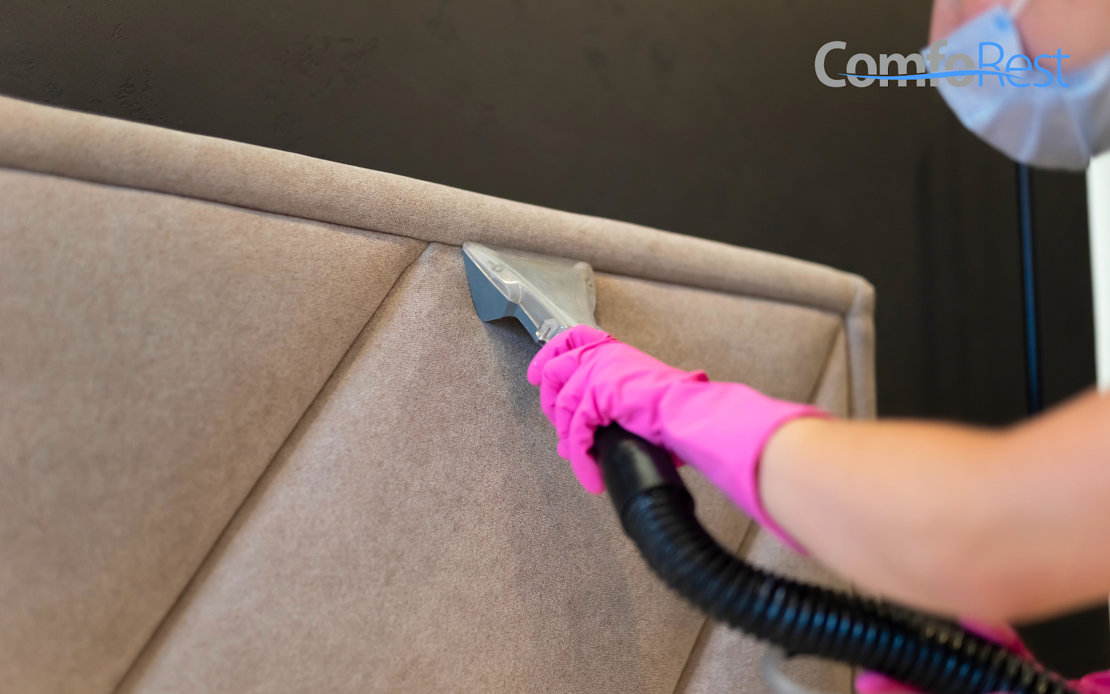 Professional cleaning of an upholstered headboard using a vacuum and protective gloves to maintain hygiene and extend durability