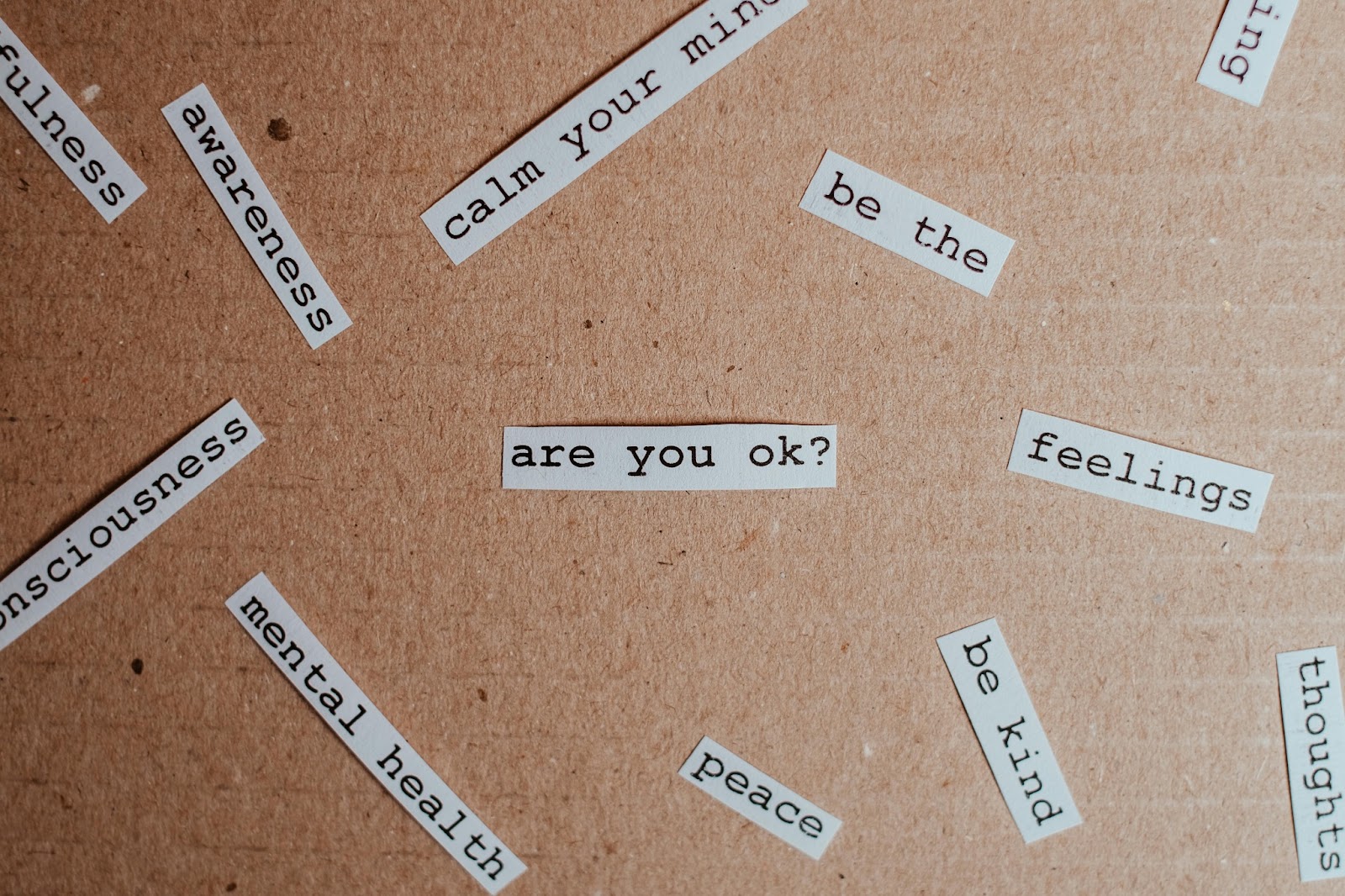 Mental health-related words and phrases like 'are you ok?', 'mental health', 'peace', and 'be kind' scattered on a brown paper background, symbolizing emotional awareness and support.