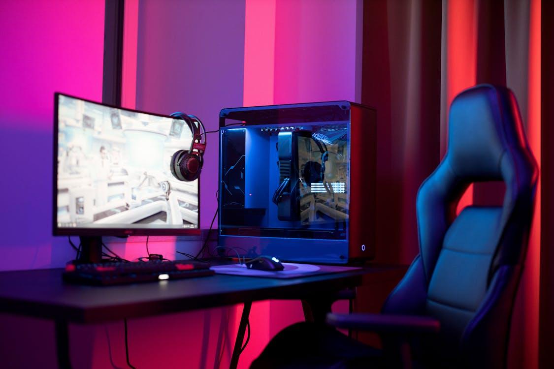 Free A sleek gaming setup featuring a high-end PC, widescreen monitor, and ergonomic chair lit by neon lights. Stock Photo