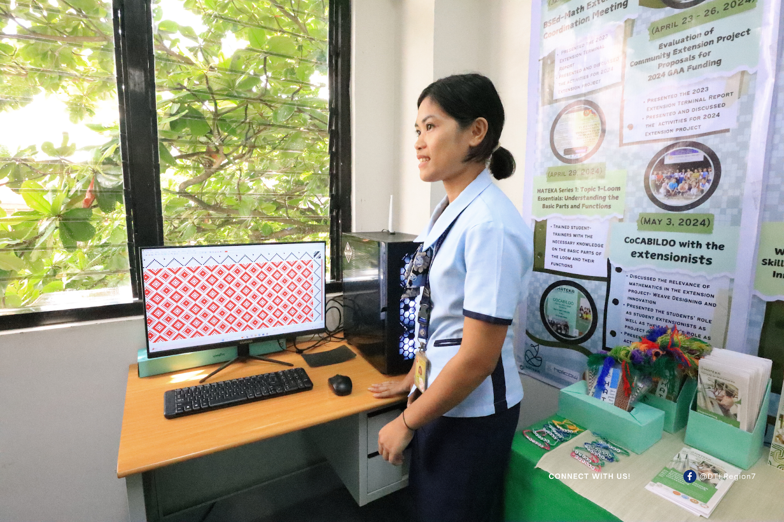 A person standing beside a computer displaying a red and white geometric pattern, with posters in the background detailing TESDA-funded skills training and livelihood projects held in April and May 2024.
