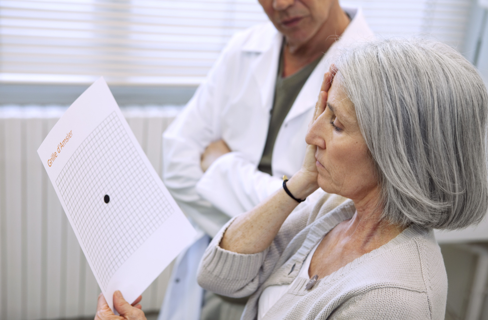 A mature patient sits and stares at an Amsler grid covering one eye.