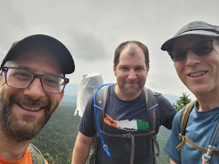 Selfie of three men smiling on the summit of a mountain.