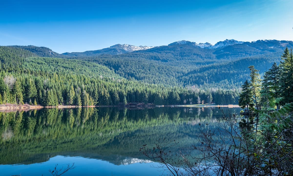 View of Lost Lake in Whistler with still waters mirroring the green mountains in the background