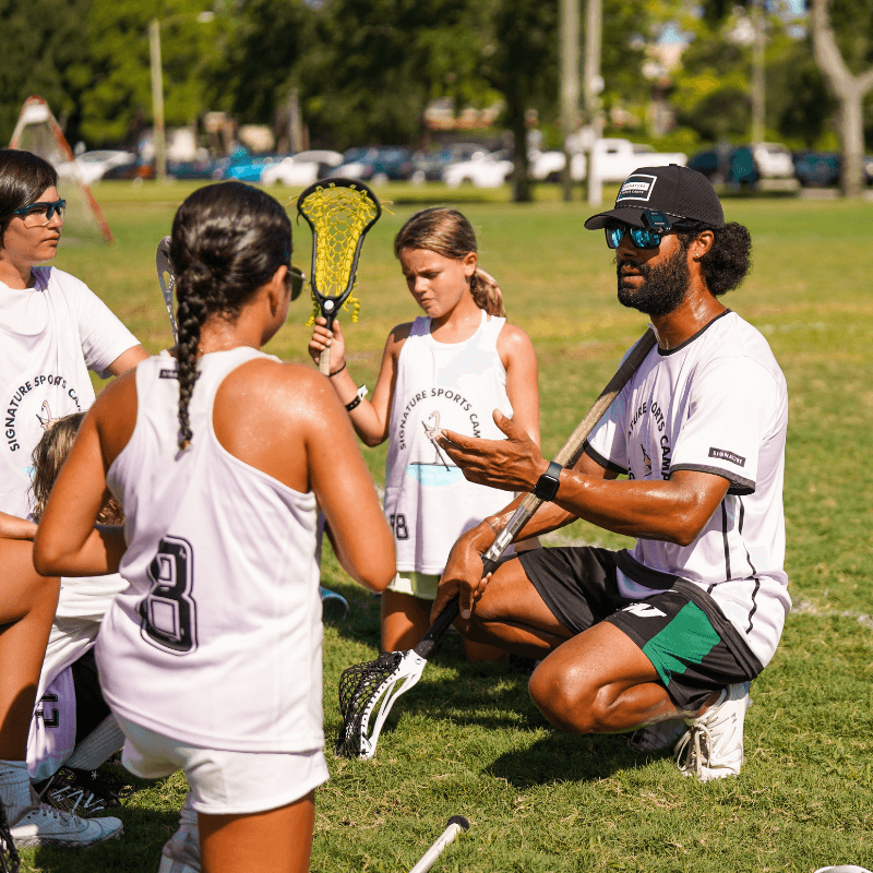 Resident Coach at signature sports camps providing feedback to a group of girls during lacrosse practice