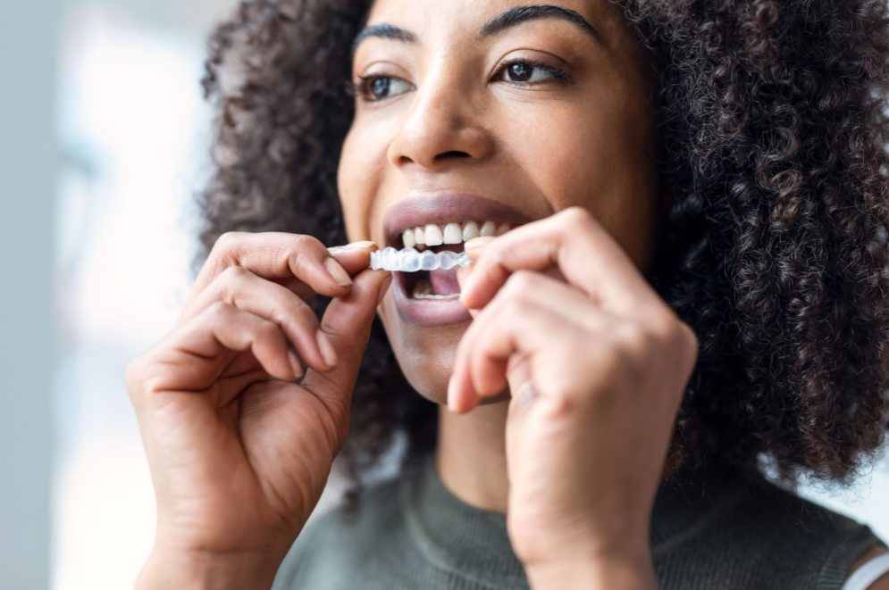 Smiling woman placing clear Invisalign aligners for discreet orthodontic care by MP Orthodontics.
