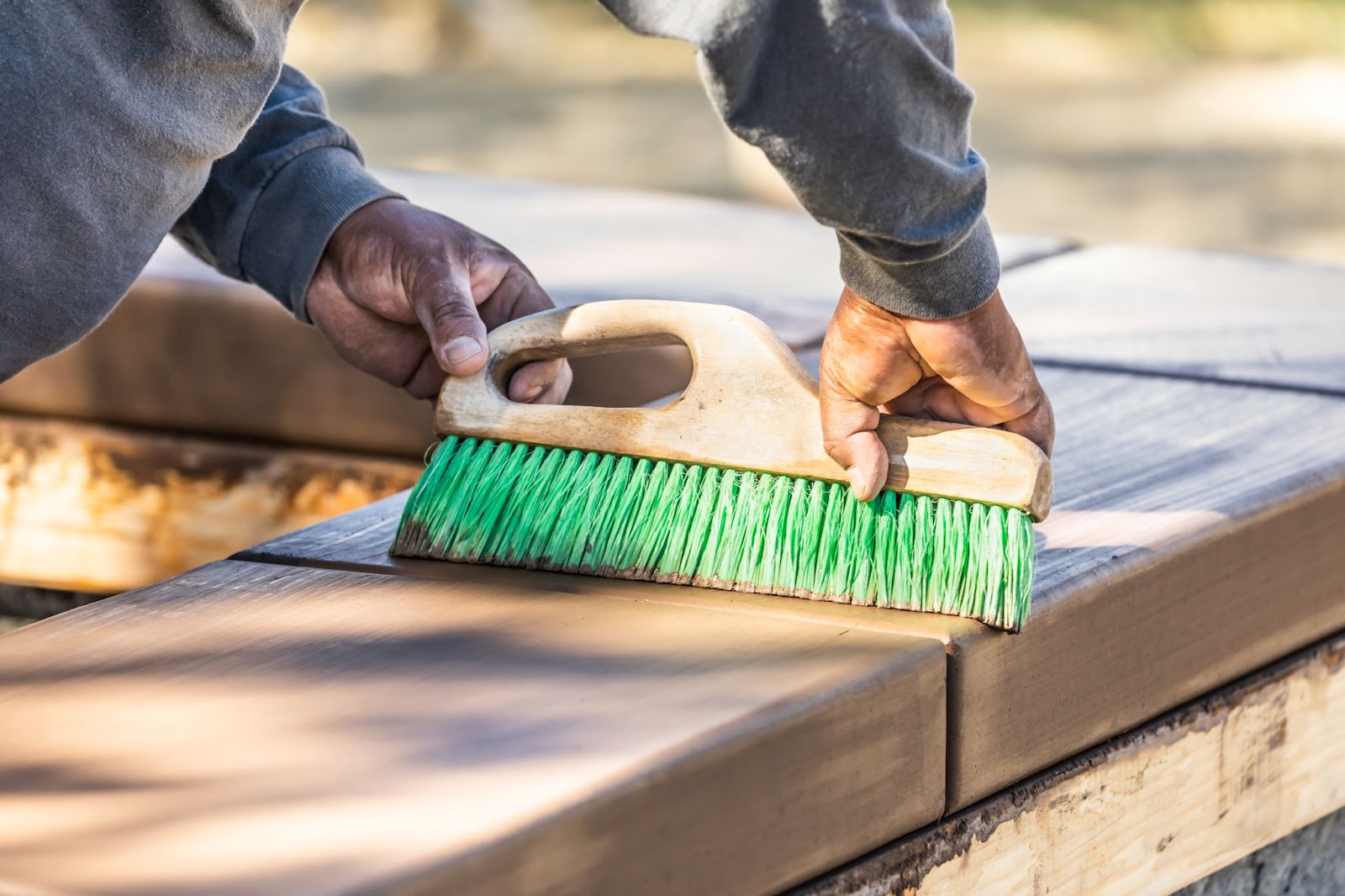 A construction worker uses a brush to create a broom-finished concrete texture on wet cement.