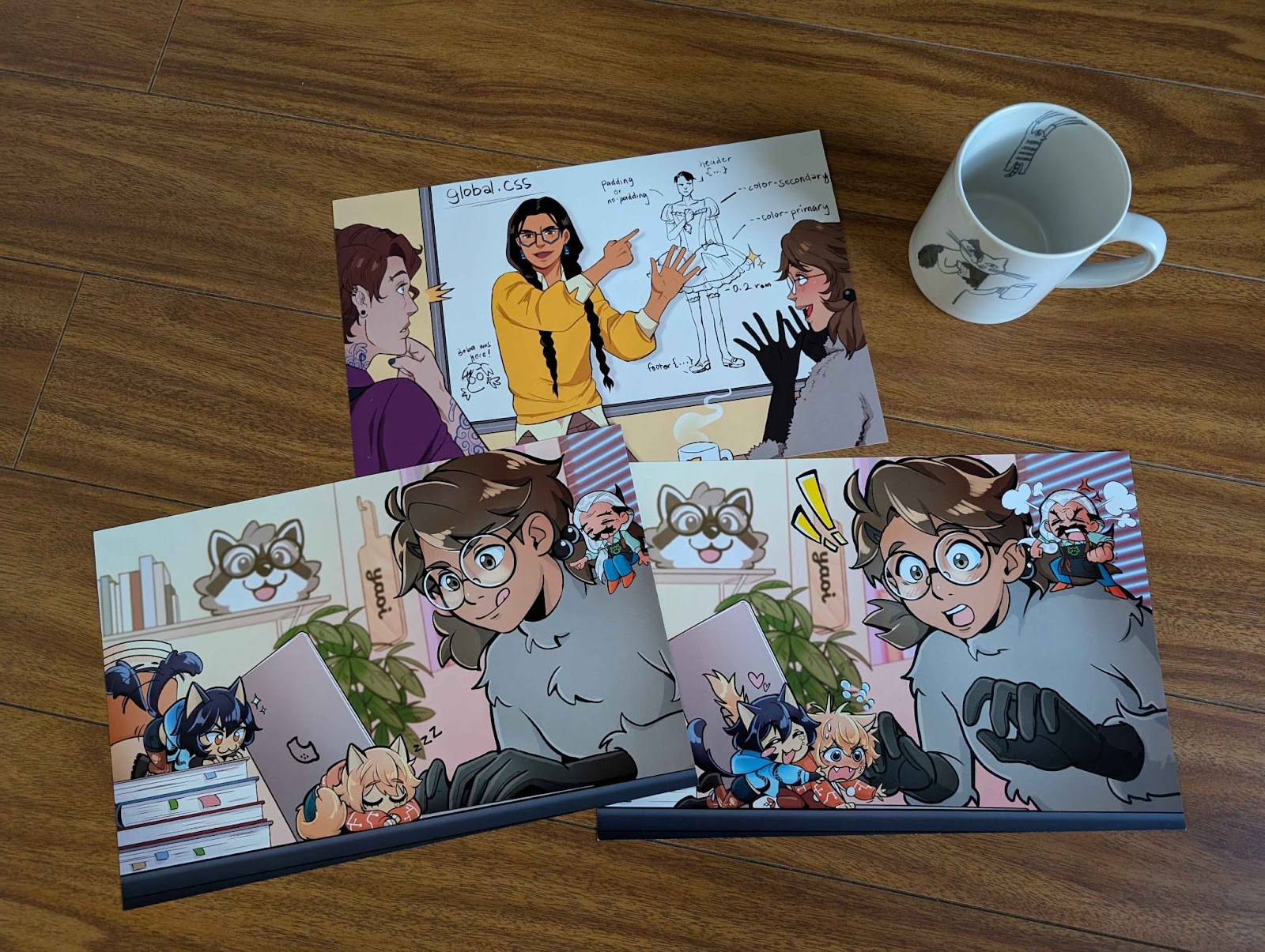 Three eight inch by twelve inch prints featuring characters from the Fujoshi Guide to Web Development. A coffee mug in the corner gives a sense of the prints’ size.