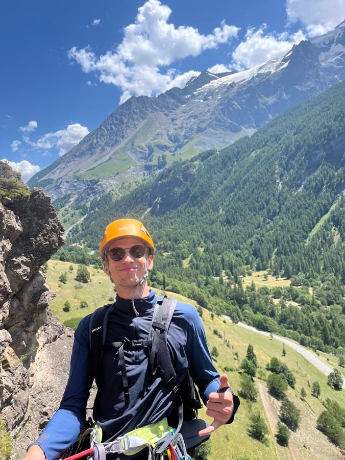 A person wearing a helmet and standing on a rock with a mountain in the backgroundAI-generated content may be incorrect.