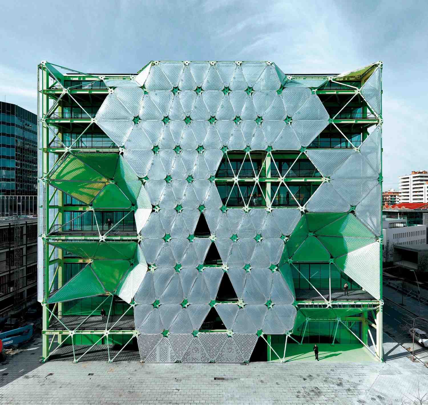 A modern building with a striking geometric facade featuring large, translucent, angular panels shaded green showcases innovative facade designs.