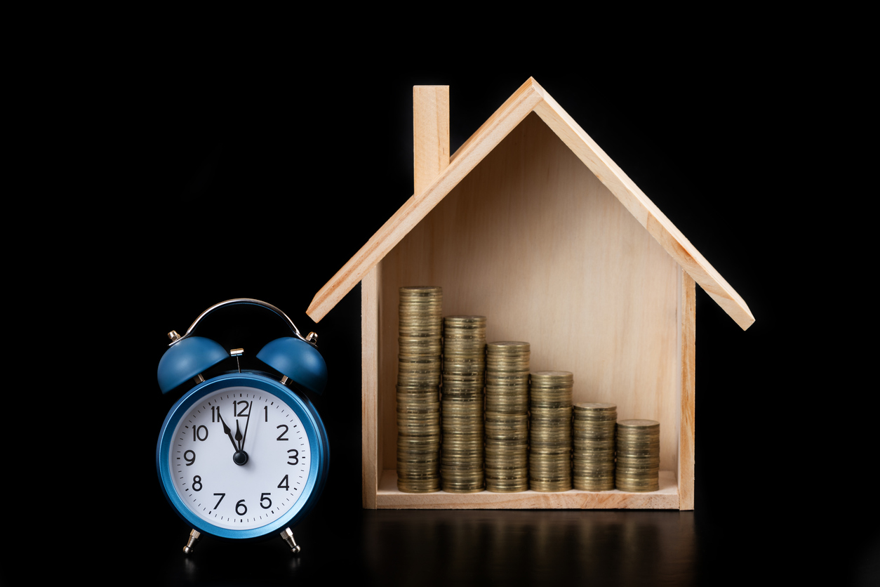 Conceito de casa e moedas com relógio despertador em fundo preto, representando investimentos em renda fixa.
