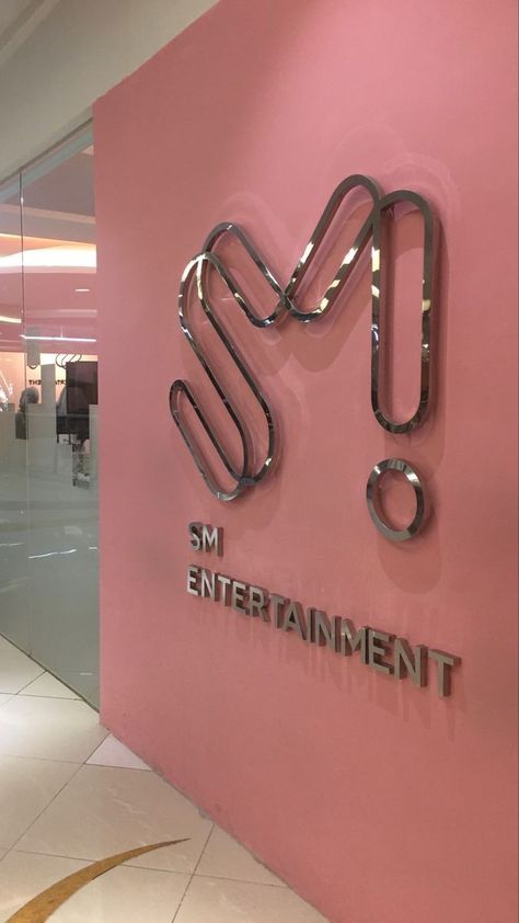 This contains an image of the entrance Sm Entertainment  building with pink walls and shiny metal letters that read sm entertainment