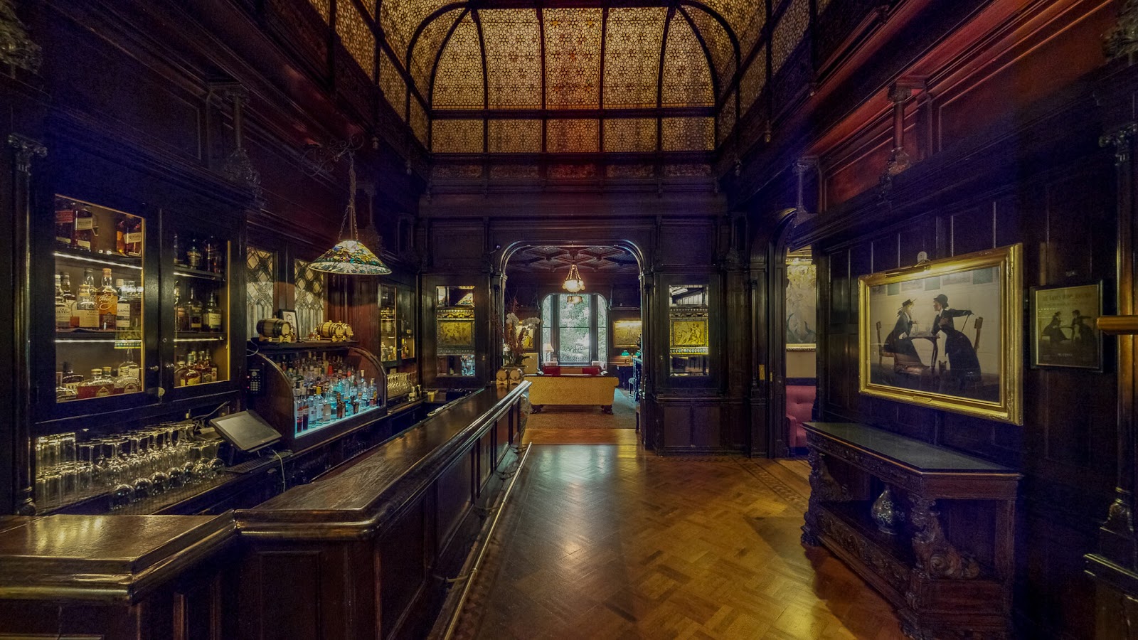 Elegant vintage bar interior with dark wood paneling, ornate glass ceiling, classic liquor display, and framed artwork at the National Arts Club in New York City.
