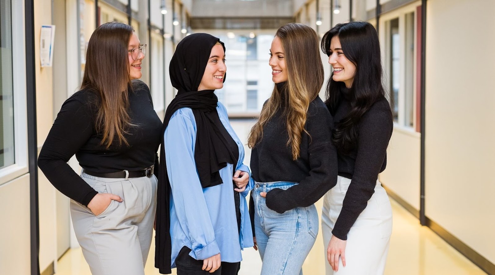 Équipe de jeunes femmes nutritionnistes-diététistes professionnelles souriantes discutant dans un couloir, illustrant la collaboration et la diversité chez ÉquipeNutrition.