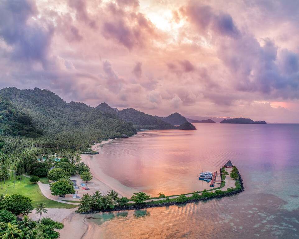 Pink and purple sky reflecting on water surrounded by greenery.