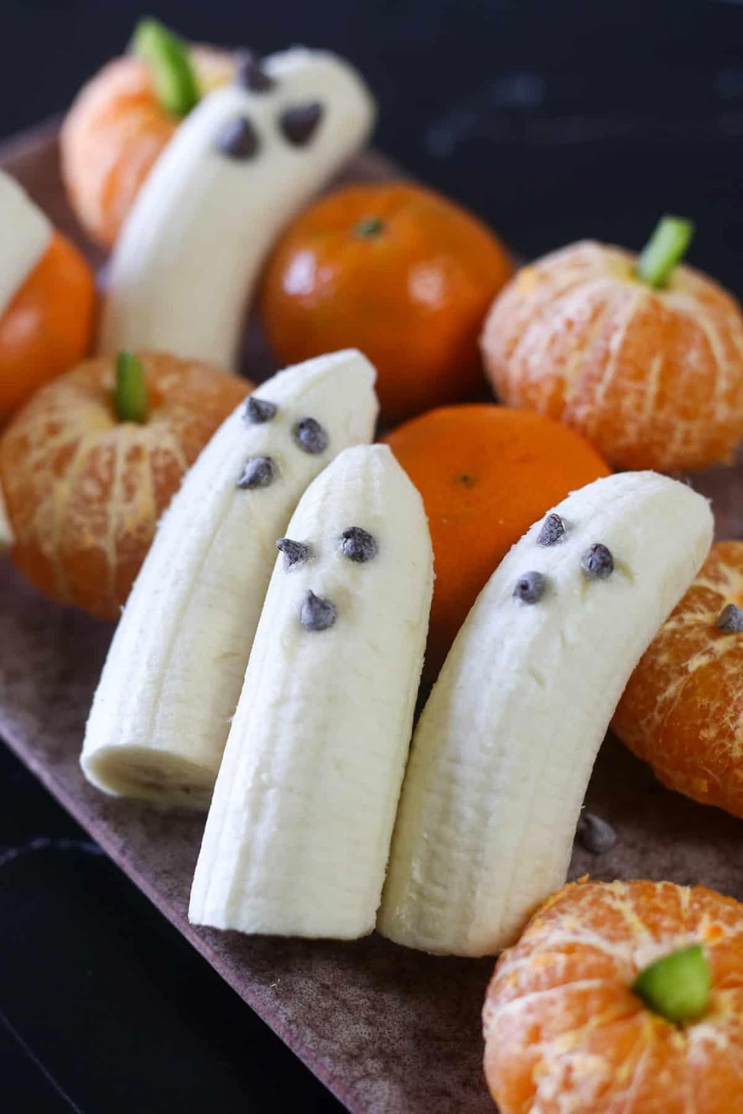 Ghost bananas on a plate with clementine pumpkins. 