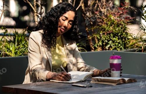 Young woman on table writing on notebook and holding a cup of coffee.