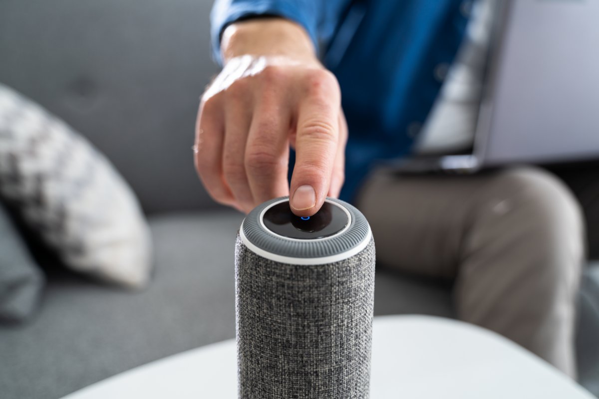 Hand pressing button on a smart speaker for voice assistant activation.