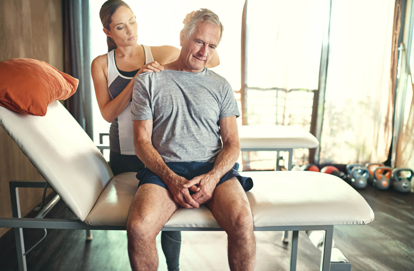 An adult during physiotherapy smiling in front of a window while a physiotherapist helps them with neck pain due to whiplash injury.