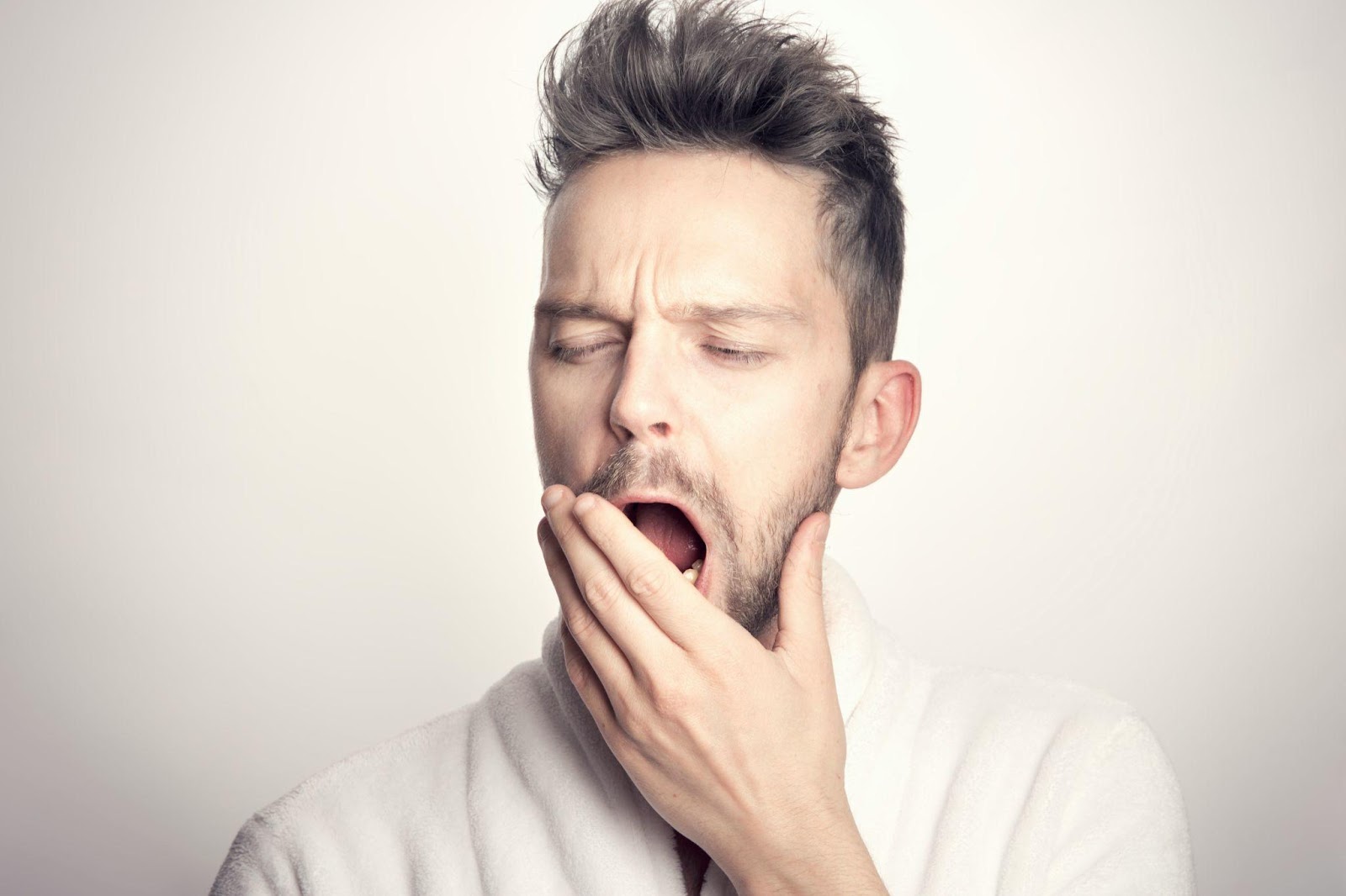 a man wearing a white robe yawning with his hand in front of his mouth