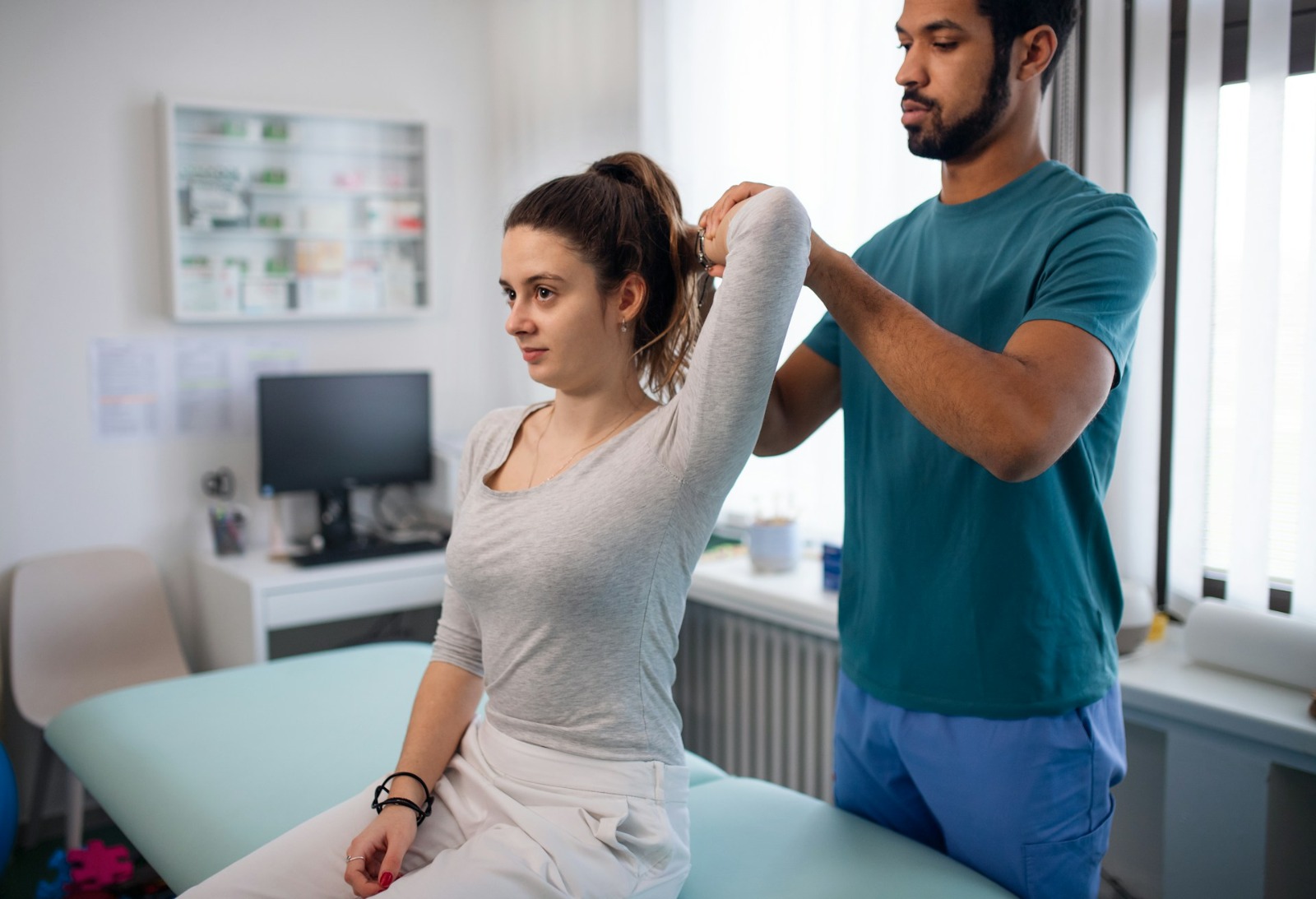  A physical therapist assists a woman by stretching her arm in a clinical setting. This suggests physical therapy or exercise as a method to alleviate burnout.