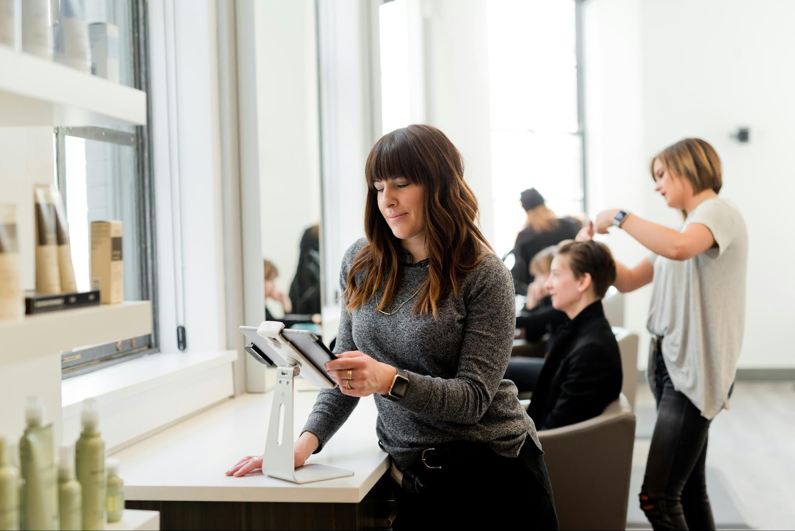 Salon stylist checking tablet while another styles client’s hair