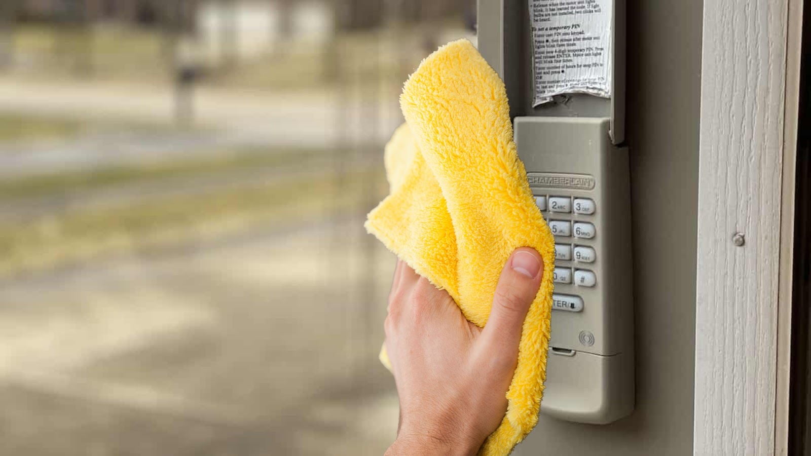 A hand cleaning the garage keypad with a damp yellow cloth