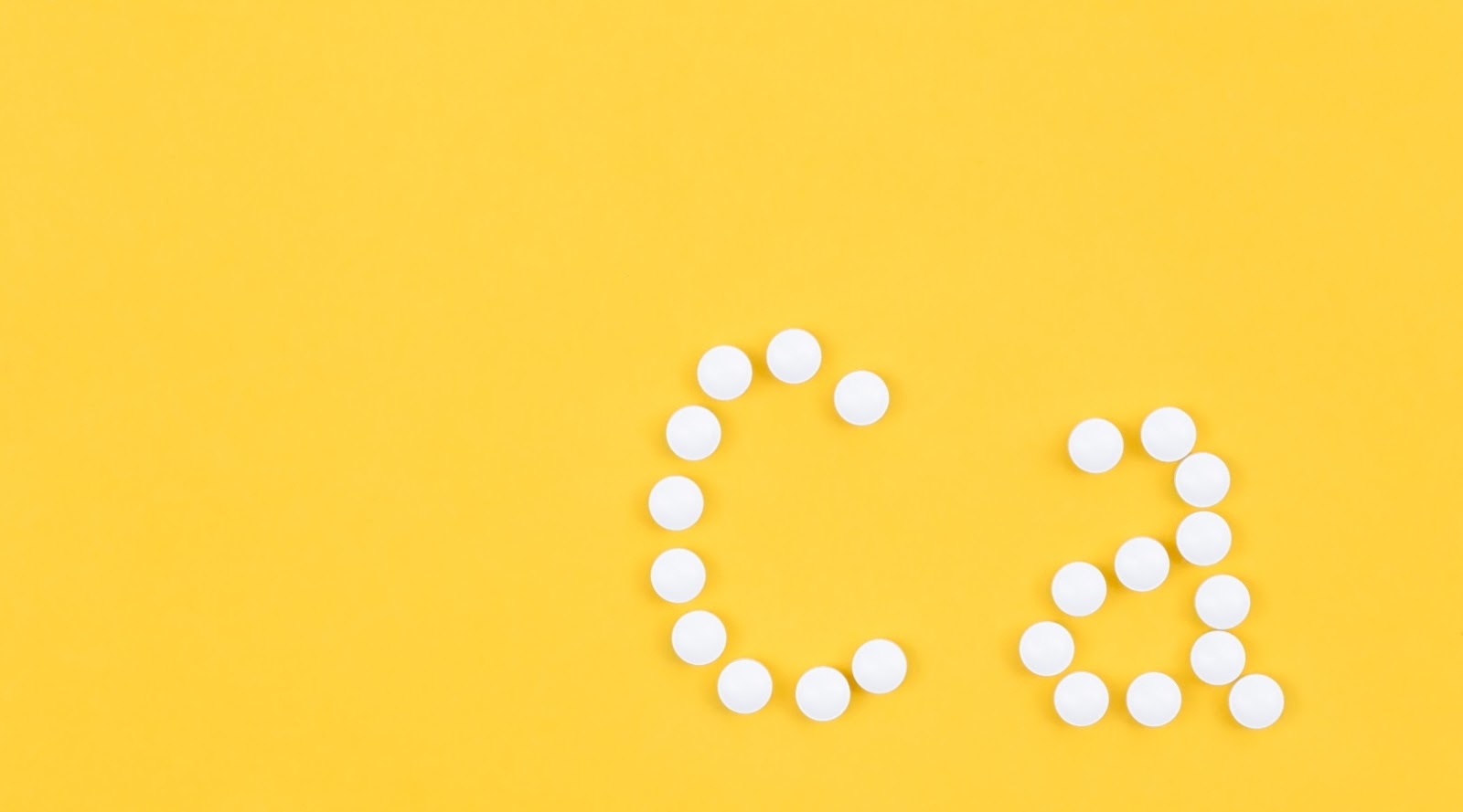 Calcium tablets are arranged to form the letters "Ca" on a bright yellow background, symbolizing calcium as an essential nutritional supplement.