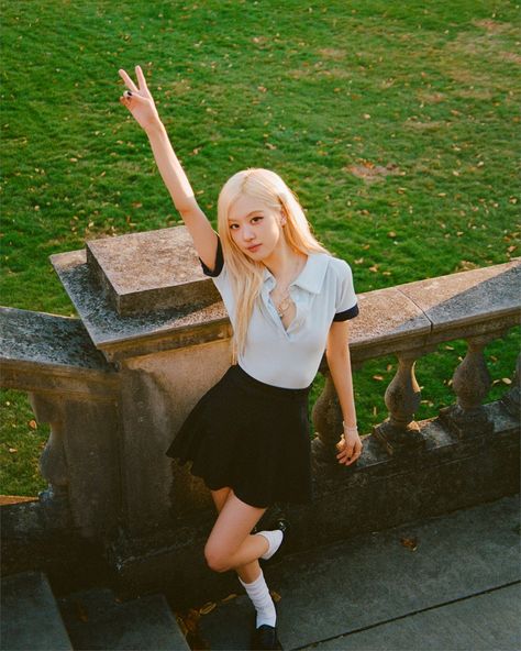 This contains an image of BLACKPINK Rosé's posing on the steps in front of a grassy area with her hand up