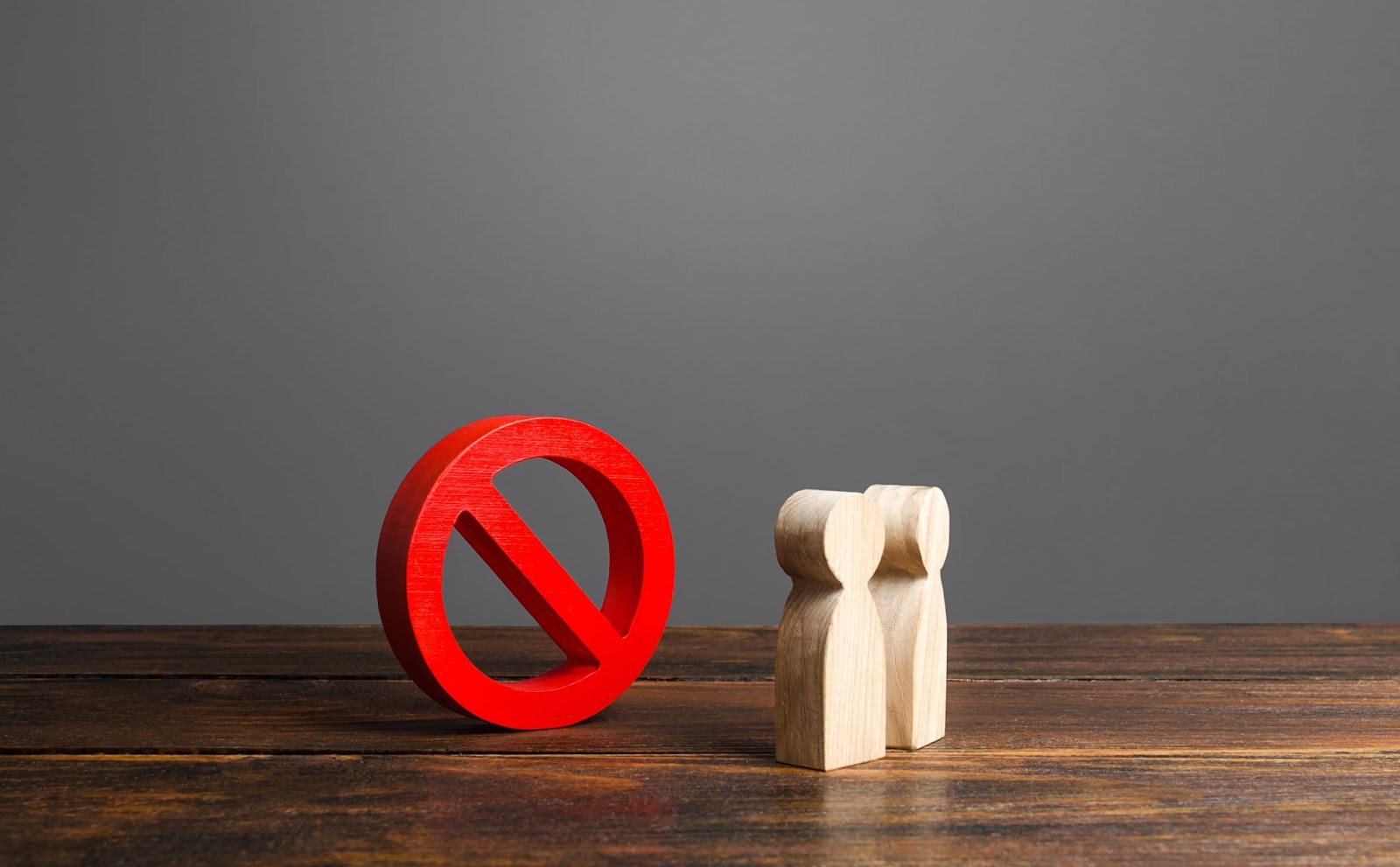 Stop sign next to two wooden cutouts of people on a wooden surface. 