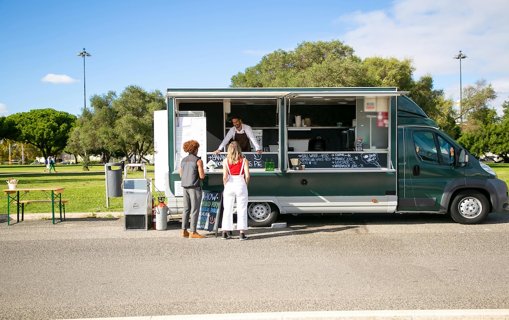 two people standing outside a food truck ordering food