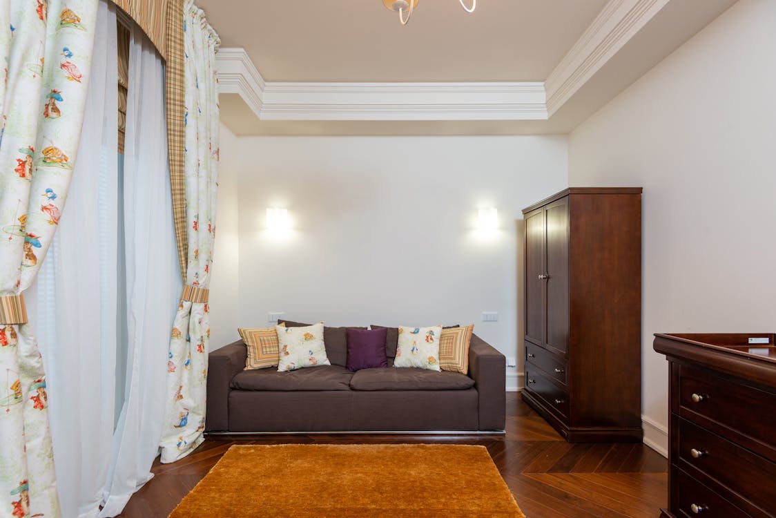 Free Modern living room featuring a dark sofa, floral curtains, and wooden furniture in a cozy setting. Stock Photo