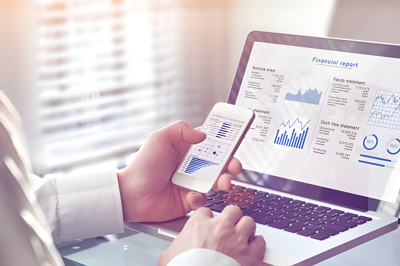 Accountant using a smartphone and laptop to review financial reports, symbolizing the challenge of adapting to new accounting software and technology.