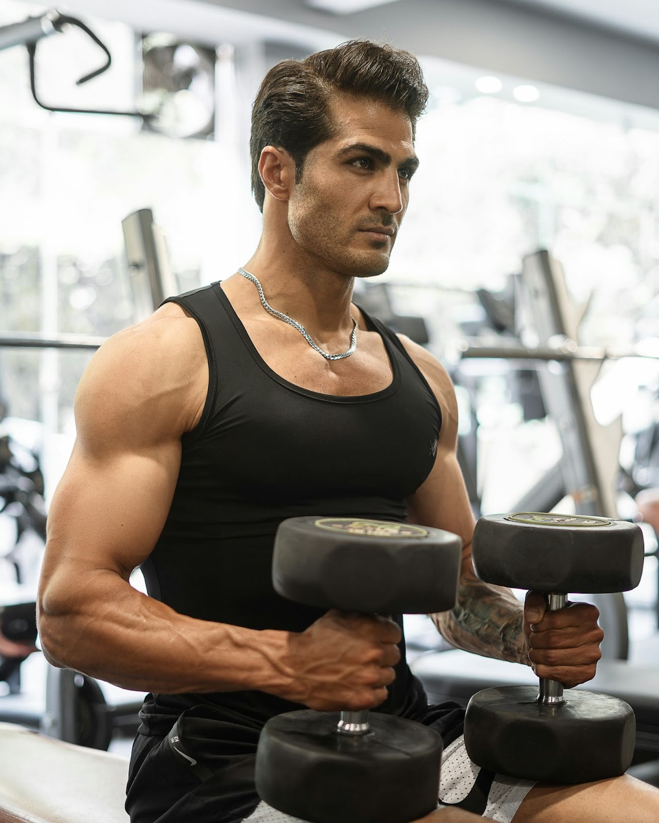 A man wearing a black tank top holding weights in the gym.