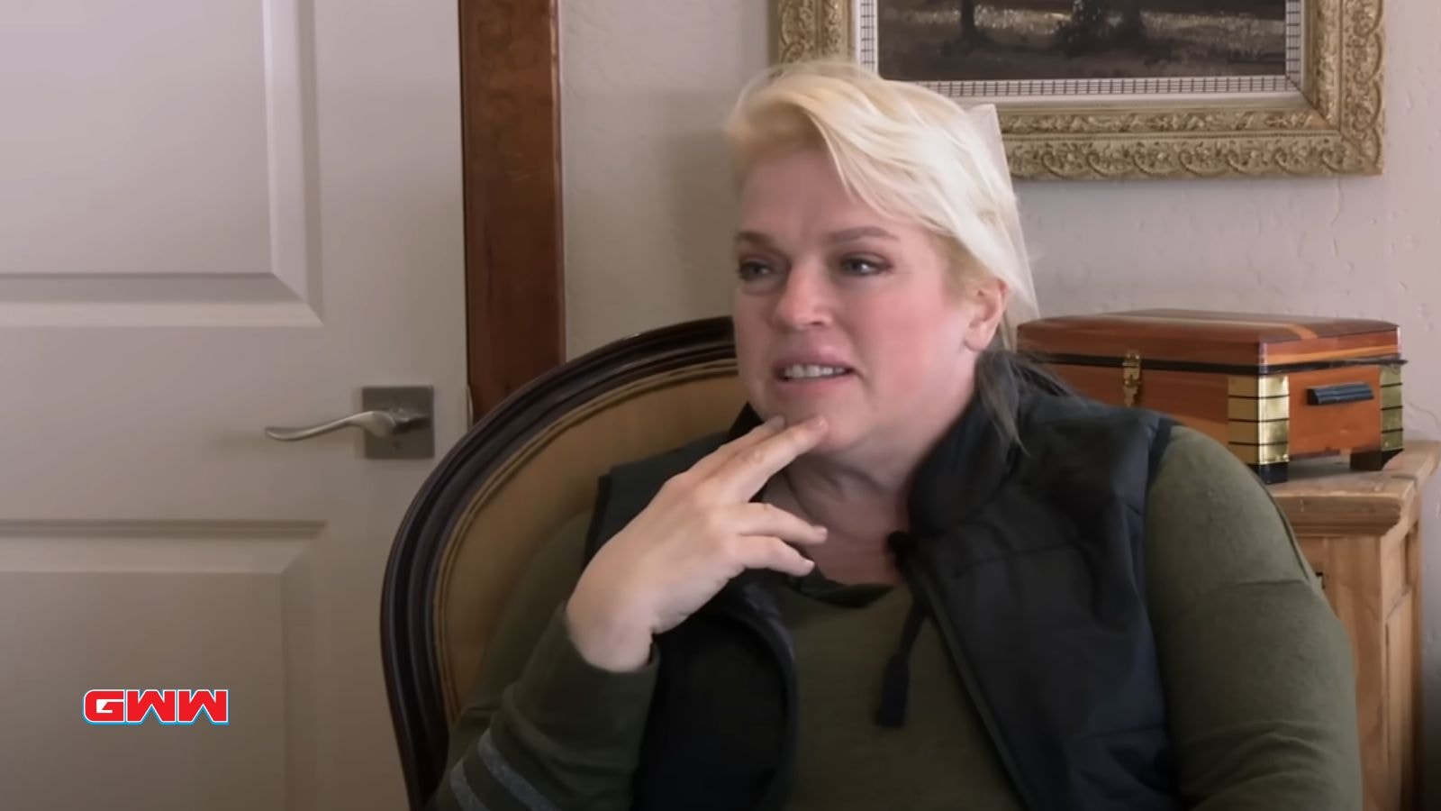 Janelle Brown with short blonde hair wearing a dark vest, sitting indoors.