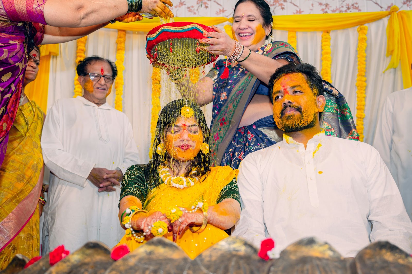 A group of people pouring handi on an Indian bride and groom.